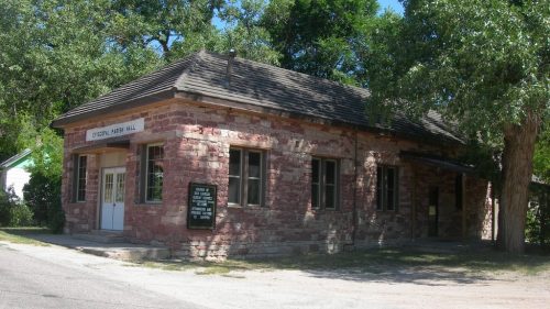 Historic stone building with a sloped roof, surrounded by trees, featuring a sign that reads "Cypress Mill Hall."