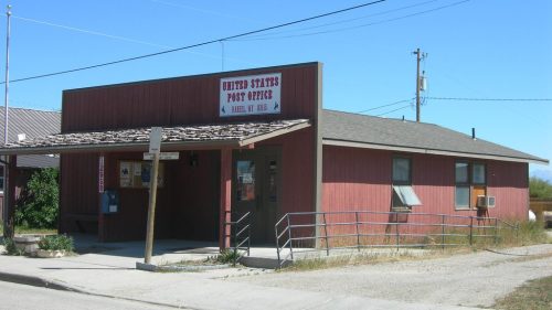 A small, red wooden building with a sign reading "United States Post Office" under a clear blue sky.