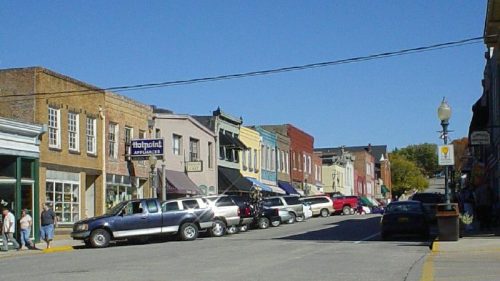 A quaint street lined with colorful storefronts and parked cars under a clear blue sky.