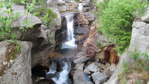 A serene waterfall cascades over rocky formations, surrounded by lush greenery and smooth stones.