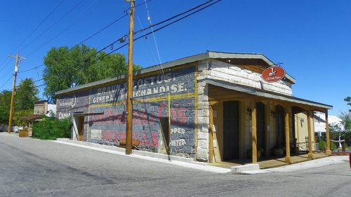 A historic general store with a faded mural, set against a clear blue sky and power lines in a small town.
