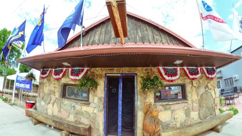 A rustic stone building with a red roof, decorated with flags and bunting, featuring an "Open" sign at the entrance.