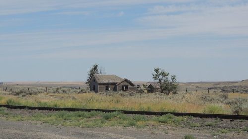 Abandoned house in a vast, open landscape with sparse vegetation and a clear blue sky.