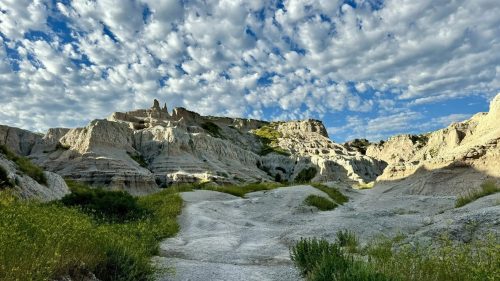 A scenic landscape featuring rugged rock formations, green grass, and a dramatic sky filled with clouds.