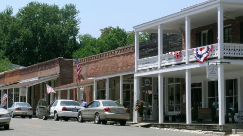 Historic street lined with brick buildings, shops, and American flags, under a clear blue sky.