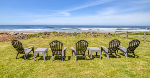 A long row of outdoor chairs sits on a grassy lawn, facing the Pacific Ocean.