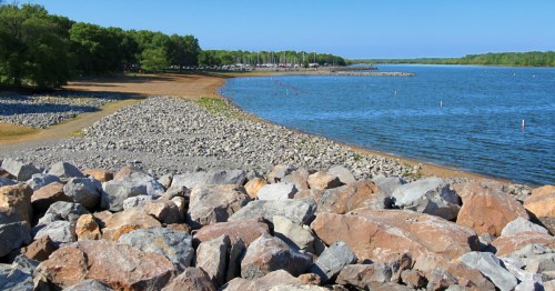 A golden sand beach between a rocky shorline and a forested cove at Carlyle Lake, the best lake in Illinois for shallow swimming.