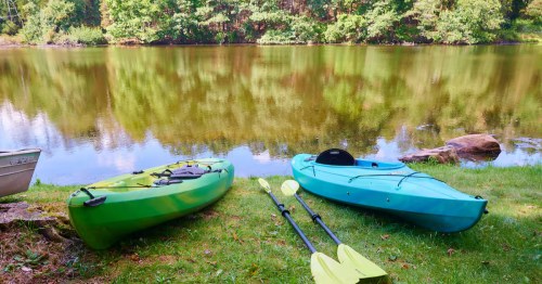 A green and a blue kayak sit in the grass next to the lake at the Lakefront Cabin Airbnb in Blairstown, New Jersey.
