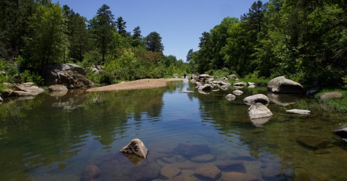 Boulders sit in a river surrounded by green trees.