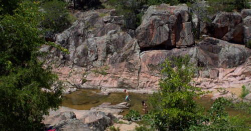 Two people walk through a stream surrounded by rock formations.