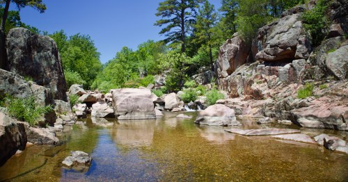 Rock formations and green trees surround a pool of water.