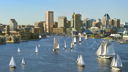 A scenic view of a city skyline with sailboats on a river under a clear blue sky.