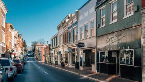 A charming street lined with shops and boutiques, featuring a clear blue sky and parked cars along the curb.