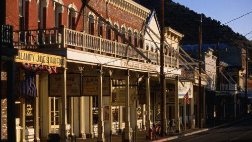 Historic buildings line a street in a western town, with flags and signage under warm evening light.