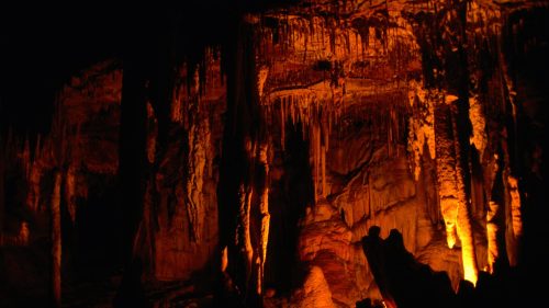 Stalactites and stalagmites illuminated in warm orange light inside a dark cave.