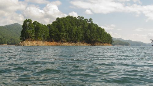 A kayak with gear in the foreground, facing a lush green island surrounded by calm water and mountains in the background.