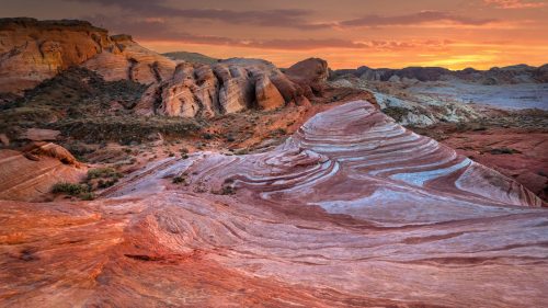 Vibrant sunset over colorful rock formations in a desert landscape, showcasing layered textures and hues.
