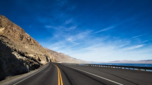 A winding road alongside a rocky landscape under a clear blue sky.