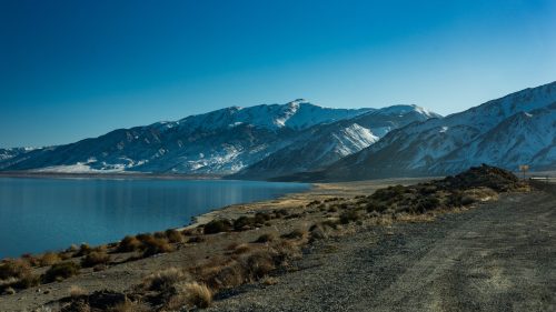 A serene landscape featuring snow-capped mountains beside a calm lake under a clear blue sky.