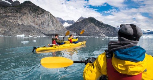 A group of friends enjoys ocean kayaking near a glacier during their vacation trip in Alaska.