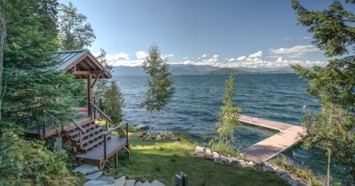 The exterior of a lakefront Airbnb in northern Idaho with a small grassy area and an L-shaped private dock.