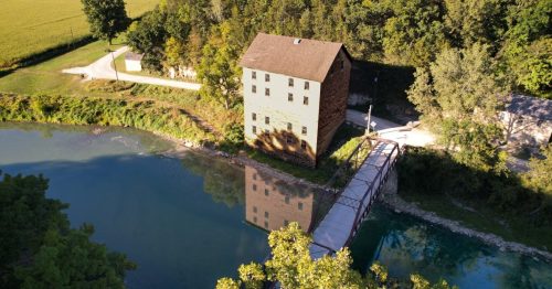 An aerial, river shot of Elkader and the Motor Mill with green foliage, an outdoorsy town in Iowa