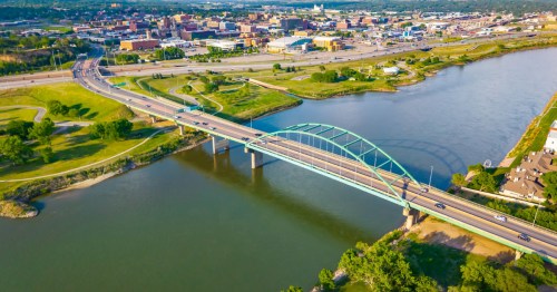 An aerial view of the city by the river with a big blue road bridge, in Sioux City, a walkable city in Iowa.