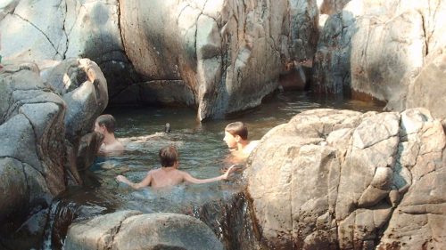 Four people enjoying a natural pool surrounded by large rocks and flowing water.
