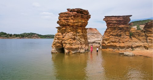 A woman and child standing in the water at Wilson Lake between two golden, rock tower natural formations. This cove is near Lucas, Kansas.