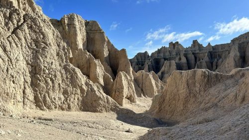 A rugged landscape of eroded rock formations under a blue sky, showcasing dramatic cliffs and valleys.