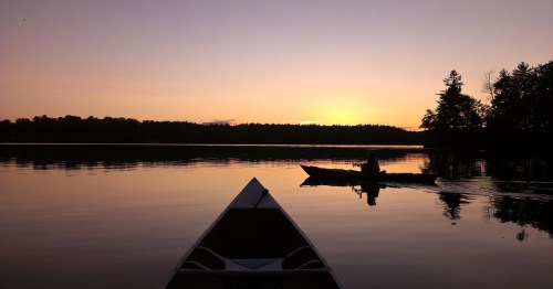 A kayak and canoe float on a calm lake at sunset near Monmouth, Maine.