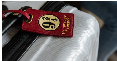 A red Hogwarts luggage tag attached to the handle of a silver suitcase. The perfect bag for Checking into a Harry Potter themed Airbnb in Missouri.