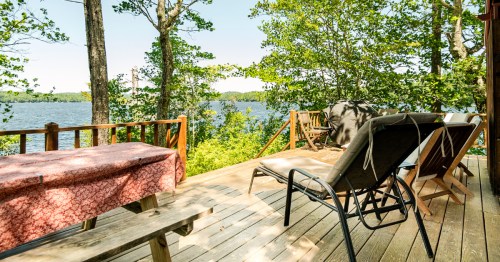 Rustic deck with picnic table and loungers facing the lake at a private island cabin in Raymond, Maine.