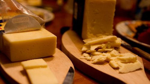 Two blocks of cheese on wooden boards, one partially sliced and the other crumbled, with knives nearby.