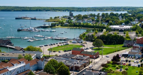 An aerial view of Downloaded the harbor and town of Rockland, Maine. Boats line the harbor and the streets are walkable in every direction.