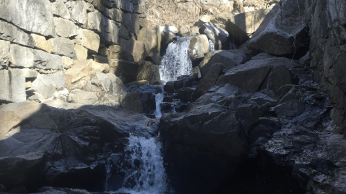 A serene waterfall cascading over rocky terrain, surrounded by stone walls and natural scenery.