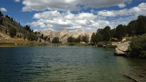 A serene lake surrounded by mountains and trees under a partly cloudy sky.