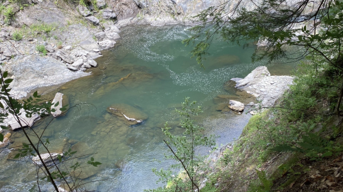 A serene river flows through a rocky gorge, surrounded by lush greenery and steep cliffs.