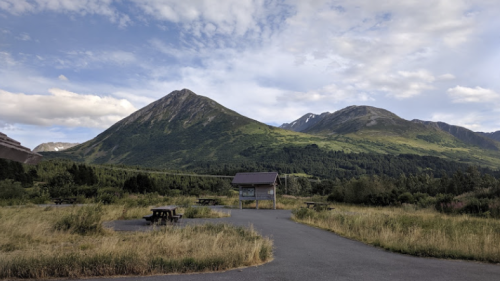 Scenic view of mountains under a blue sky, with a picnic area and grassy landscape in the foreground.