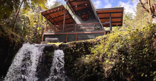Looking up at a waterfront Airbnb in Hawaii that overlooks a small waterfall.