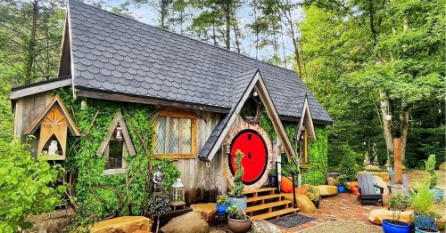A tiny home in the woods with ivy covered walls and a round, red door at themed Airbnb in Tennessee