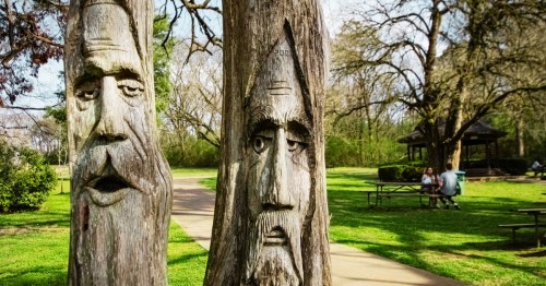 A pair of faces of old men carved into tree trunks in a park in Montevallo, Alabama.