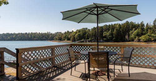 Shaded deck with umbrella and table overlooking the cove at a water's edge cottage in Harpswell, Maine.