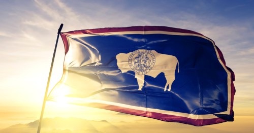Wyoming state of United States flag waving on the top sunrise mist fog.