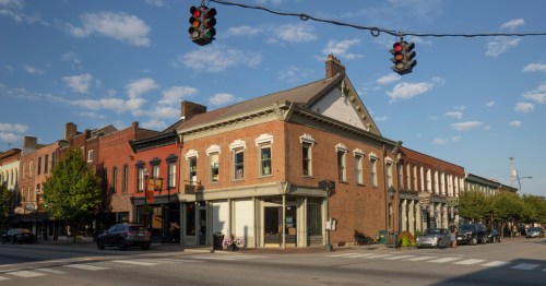 Downtown Bardstown, Kentucky with preserved brick storefronts, historic commercial buildings, parked cars, and a charming small-town streetscape beneath a blue sky.