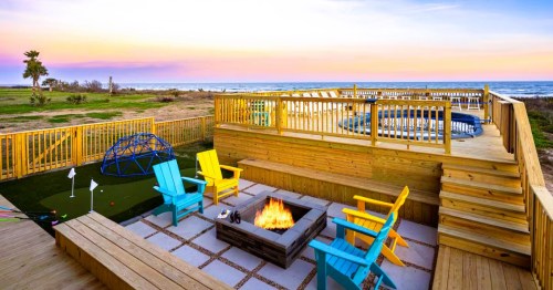 Views of a pool deck with a fire pit and colorful chairs, overlooking the Gulf, at a waterfront rental in TX.