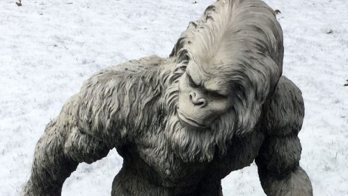 A large, gray yeti statue with muscular features walking on snow-covered ground.