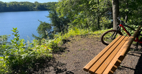 A wooden park bench and mountain bike look out over a deep blue lake in Cuyuna Country, Minnesota.