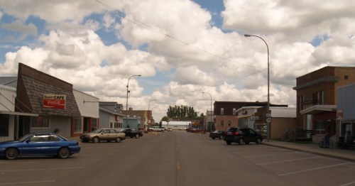 Empty wide main street downtown in Cavalier North Dakota with parked cars under a blue sky.