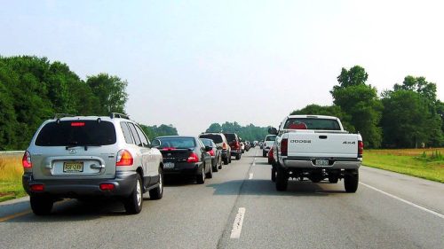 Traffic jam on a highway with multiple vehicles lined up, surrounded by green trees and open fields.